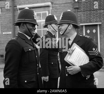 Er wird neun Tage lang als erster schwarzer Polizist in London, PC Norwell Gumbs, 21, am Metropolitan Police Training College in Hendon, London ausgebildet, da ihn Station Sgt John Aldridge auf die richtige Weise anweist, seinen Helm zu tragen. Stockfoto