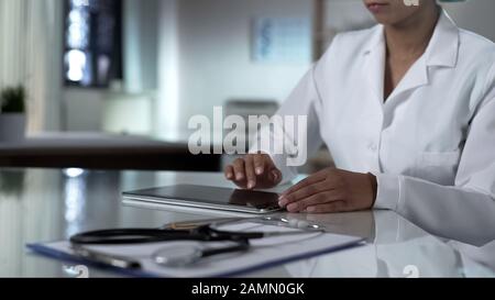 Weibliche Ärztin scrollt Tablettenbildschirm, prüft die Testergebnisse der Patienten, Klinik Stockfoto