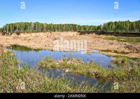 Entwicklung von Sandbruch. Bagger und Bergbaugeräte in der Ferne. Überschwemmte verbrachten einen Teil des Steinbruchs. Gewinnung von Sand und Baumaterial Stockfoto