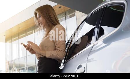 Nette Geschäftsfrau, die den Kunden auf dem Smartphone anruft und in der Nähe des Automobils steht Stockfoto