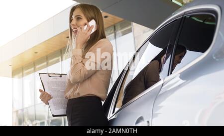 Lady Broker mit Vertrag im Gespräch mit dem Kunden auf dem Smartphone, in der Nähe des Autos Stockfoto