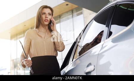 Selbstbewusste Geschäftsfrau, die mit dem Kunden in der Nähe eines geparkten Autos auf dem Smartphone spricht Stockfoto