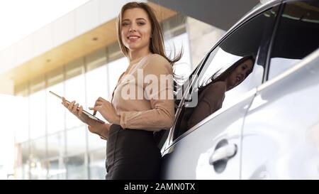 Hübsche Geschäftsfrau hält Tablet, steht in der Nähe des Autos und posiert für die Kamera Stockfoto