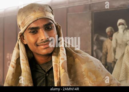 Der Mann, der nur Kopftuch und Hals trägt, sollte mit einem Tuchschutz ausgestattet sein, um Zementsäcke von Zug zu Lkw in Mathura, Indien, zu bewegen. Stockfoto
