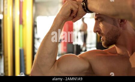 Passen Sie das Männchen, das seine entwickelten Muskeln bewundert, und machen Sie ein Fitness-Studio mit Bikepose, stolz auf das Ergebnis Stockfoto