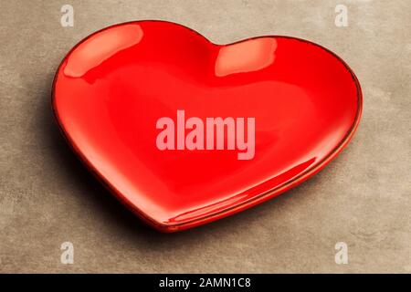 Eine rote, herzförmige Platte auf grauem Betonhintergrund. Dekoration für Valentinstag, Hochzeit, Geburtstag einer anderen Liebesfeier. Stockfoto