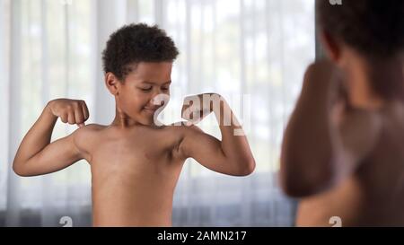 Süßer afrikanischer Junge mit Armmuskeln im Vorderspiegel, Sportkraft, Gesundheitspflege Stockfoto