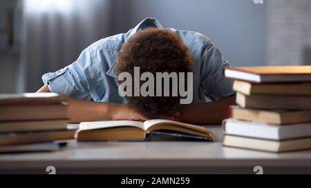 Das männliche Kind, das auf dem Tisch schläft, hat es satt, Bücher zu lesen und viel Hausaufgaben zu machen Stockfoto