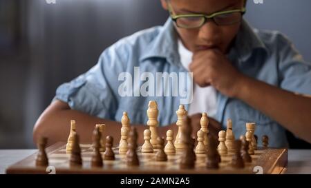 Konzentrierter Schuljunge, der daran denkt, gegnerische Schachfiguren anzugreifen und einzufangen Stockfoto