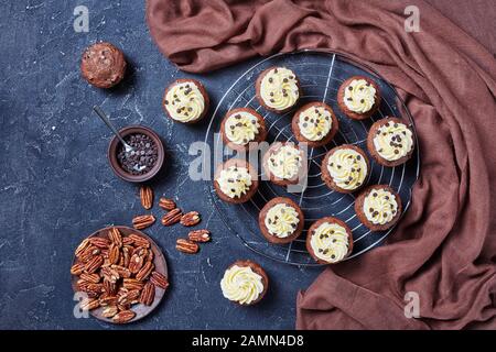 Schokoladenkuchen mit Buttercremefarben-Verwirbelung auf einem Metallkuchengestell auf einem Betontisch, horizontale Ansicht von oben, flacher Lay Stockfoto