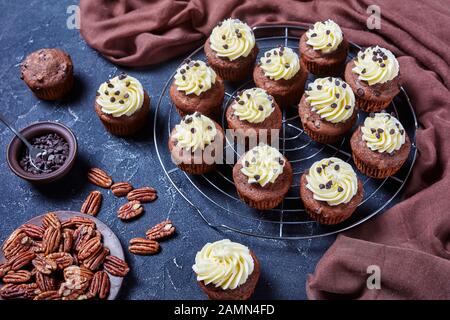 Schokoladenpecan Cupcakes mit Buttercremefarben-Verwirbelung auf einem Metallkuchenregal auf einem Betontisch, horizontale Ansicht von oben Stockfoto