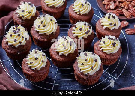 Schokoladenpecan Cupcakes mit Buttercremefarben-Verwirbelung auf einem Metallkuchenregal auf einem Betontisch, horizontale Ansicht von oben Stockfoto