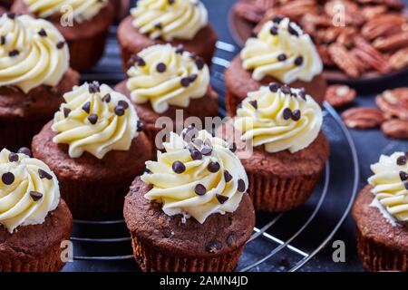 Nahaufnahme von Schokoladenpecan Cupcakes mit Buttercremefarben-Verwirbelung auf einem Metallkuchengestell auf einem Betontisch, horizontale Ansicht von oben, Makro Stockfoto