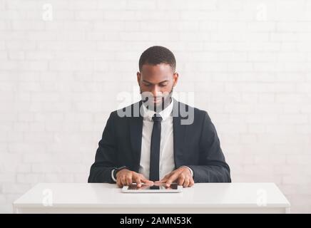 Junger moderner Geschäftsmann, der Tablet verwendet und am Arbeitsplatz sitzt Stockfoto