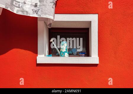 Malerische Fenster mit Gießkanne an der orangefarbenen Hauswand der berühmten Insel Burano, Venedig, Italien Stockfoto