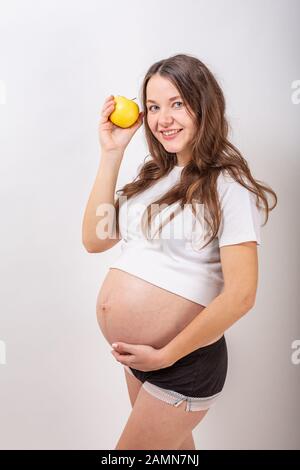 Bild der schwangeren Frau, die ihren grossen Bauch berühren und halten gelber Apfel in der Hand auf weißem Hintergrund. Stockfoto