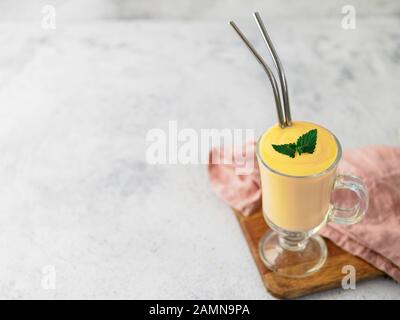 Gelbe mango Joghurt oder Smoothie auf grauem Zement Hintergrund mit Kopie Raum gelassen. Gelbwurz Lassie oder Lassi in Glas mit Metall Strohhalme Stockfoto