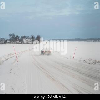 Auto auf schneebedeckter Straße in ländlicher Winterlandschaft, Schweden, Skandinavien. Stockfoto