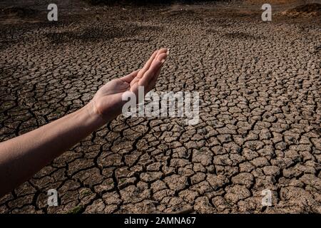 Lady Hand wartet auf Regenwasser, Gerissenen und trockenen Boden in ariden Gebieten Landschaft, Dürrekrisenkonzept Stockfoto