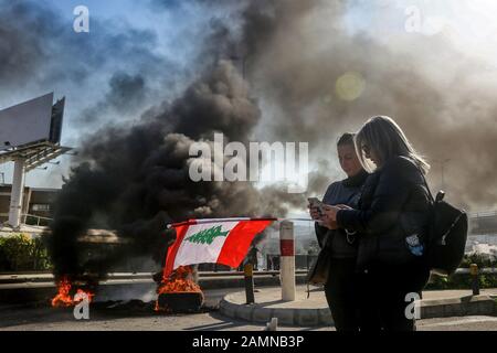 Beirut, Libanon. Januar 2020. Regierungsgegner stehen mit libanesischer Flagge vor brennenden Reifen auf einer blockierten Autobahn inmitten von Zusammenstößen mit Bereitschaftspolizisten. Libanesische Demonstranten gegen die Regierung kehrten am Dienstag für das, was sie als "eine Woche voller Wut" beschrieben haben, auf die Straßen zurück, von dem sie hoffen, dass sie Druck auf die politischen Führer ausüben werden, unter Zurückhaltung bei der Bildung einer neuen Regierung sowie der sich verschlechternden wirtschaftlichen Situation des Landes. Credit: Marwan Naamani / dpa / Alamy Live News Stockfoto