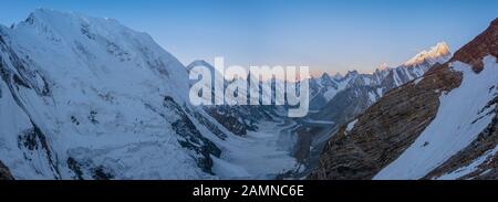 Panoramablick auf den Sonnenaufgang auf die Laila Peak Range und das Kuispang Camp auf der Spitze von Gondogoro La mit dem Biarchedi Peak auf der rechten Seite, Pakistan Stockfoto