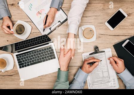 Draufsicht über Geschäftsleute, die mit Gadgets, Dokumenten und Kaffee auf dem Tisch hanteln Stockfoto