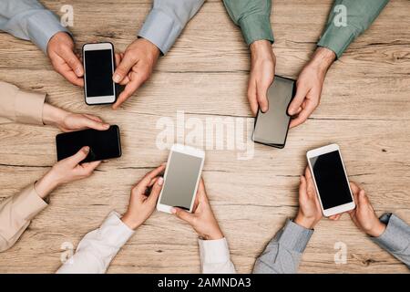 Draufsicht über Geschäftsleute, die Smartphones mit leeren Bildschirmen auf dem Tisch halten, zugeschnittene Ansicht Stockfoto