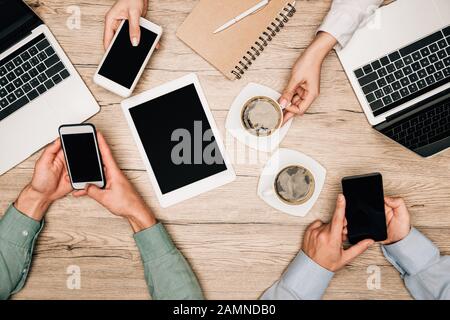 Draufsicht über Geschäftspartner mit Gadgets neben Kaffee auf dem Tisch, zugeschnittene Ansicht Stockfoto
