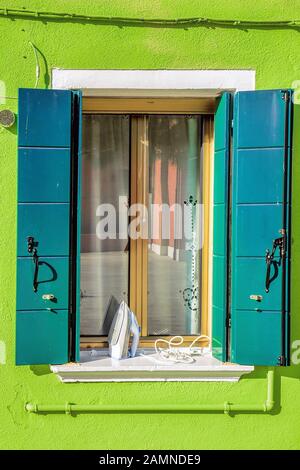 Malerisches Fenster mit flatiron an grüner Hauswand auf der berühmten Insel Burano, Venedig, Italien Stockfoto