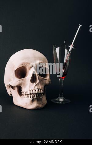 Schädel durch Weinglas mit Spritze und Blut isoliert auf Schwarz Stockfoto