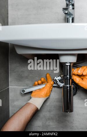 3/4-Ansicht des Reparaturwerkers in Gummihandschuhen zur Befestigung von Wasserschäden mit verstellbarem Schraubenschlüssel Stockfoto