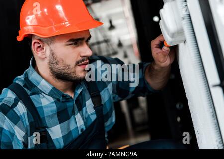 Gut aussehender Arbeiter im Sicherheitshelm, der den Lichtschalter berührt Stockfoto