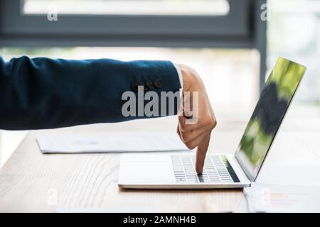 Beschnittenes Bild des Mannes, der mit dem Finger auf den Laptop auf dem Tisch zeigt Stockfoto