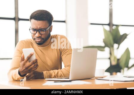 Überraschte den jungen Afro Manager, der sein Handy ansah Stockfoto