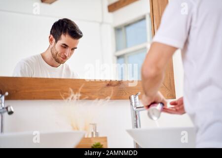 Junger Mann, der morgens die Hände im Badezimmer wascht Stockfoto