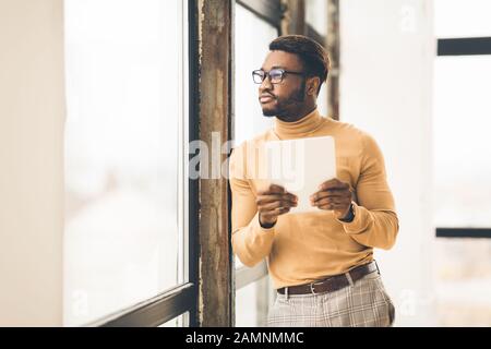 Träumender Afro Manager mit wegschauendem Tablet Stockfoto