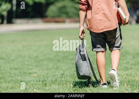 3/4-Blick auf den Schuljungen mit Rucksack auf dem Rasen im Park Stockfoto