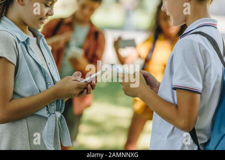 Selektive Fokussierung von Schülern, die Smartphones nutzen, während sie in der Nähe multikultureller Freunde stehen Stockfoto