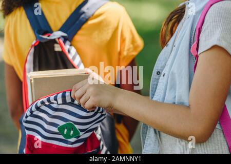 3/4-Ansicht von Schulmädchen, die Bücher im Rucksack von afroamerikanischen Freunden packen Stockfoto