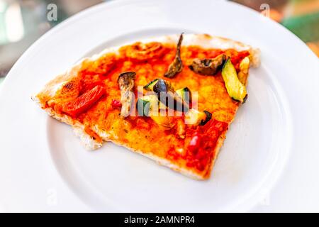 Nahaufnahme über der Makroansicht der Pizzascheibe auf weißem Teller in Italien mit veganer Tomatensauce gehackte Zucchini-Gemüse und Pilze Stockfoto