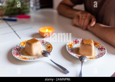 Süßes Panna Cotta Dessert mit Kerze auf dem Tisch und Löffeln und Mann im Hintergrund drinnen in Italien beleuchtet romantisches Datum Stockfoto