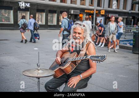 Oslo, Norway-1. August 2013: Ein Straßenmusiker tritt auf der Hauptstraße von Karl Johans Tor auf. Ein älterer charmanter Mann mit langen grauen Haaren, lächelnd a Stockfoto