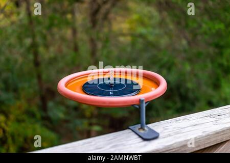 Ein kleiner Wasserbrunnen aus dem Vogelbad aus Kunststoff, der an Holzdecks in Virginia mit Waldhintergrund und Solarpanel befestigt ist Stockfoto