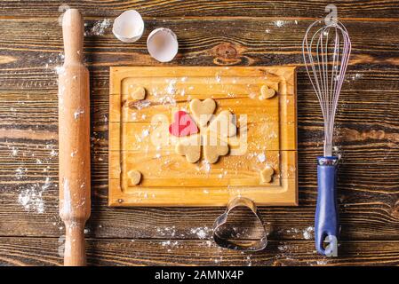 Kochende Kekse aus dem Teig in Form eines Herzens auf dunklem Holzhintergrund. Backen Sie zum Valentinstag und ein romantisches Datum Stockfoto