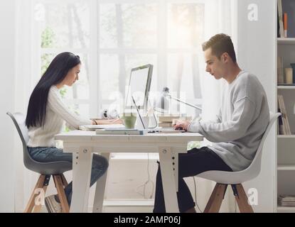 Studenten, die am Schreibtisch in der Bibliothek sitzen, studieren und verbinden sich online Stockfoto