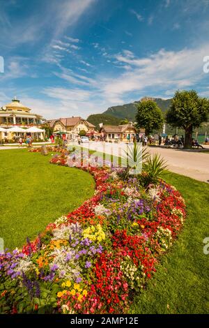 St. Gilgen, Österreich - 6 August, 2019: Park mit schönen Blumenbeet und Wolfgangsee Promenade voller Touristen an einem sonnigen Sommertag Stockfoto