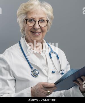 Selbstbewusste Chefärztin posiert und lächelt, sie hält eine Zwischenablage mit medizinischen Aufzeichnungen, Medizin und Gesundheitskonzept Stockfoto