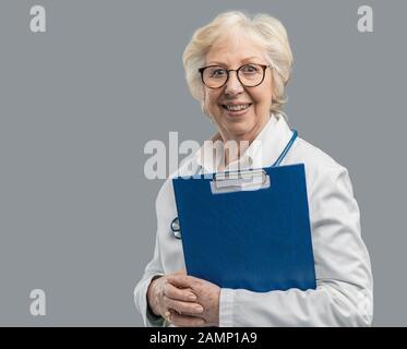 Selbstbewusste Chefärztin posiert und lächelt, sie hält eine Zwischenablage mit medizinischen Aufzeichnungen, Medizin und Gesundheitskonzept Stockfoto