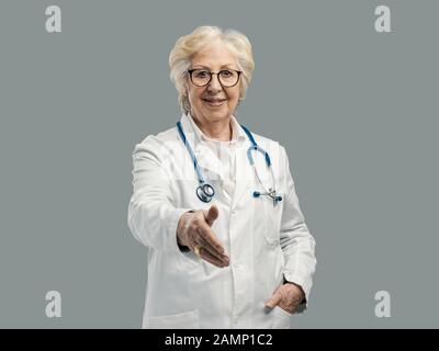 Lächelnd selbstbewusster Oberarzt lächelnd und dem Zuschauer einen Handschlag zu geben, Blickpunkt erschossen Stockfoto