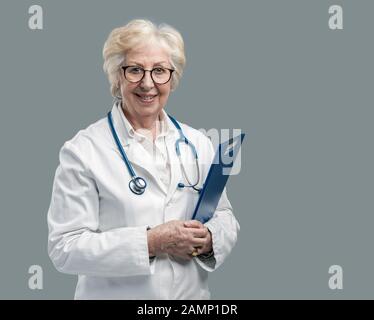 Selbstbewusste Chefärztin posiert und lächelt, sie hält eine Zwischenablage mit medizinischen Aufzeichnungen, Medizin und Gesundheitskonzept Stockfoto